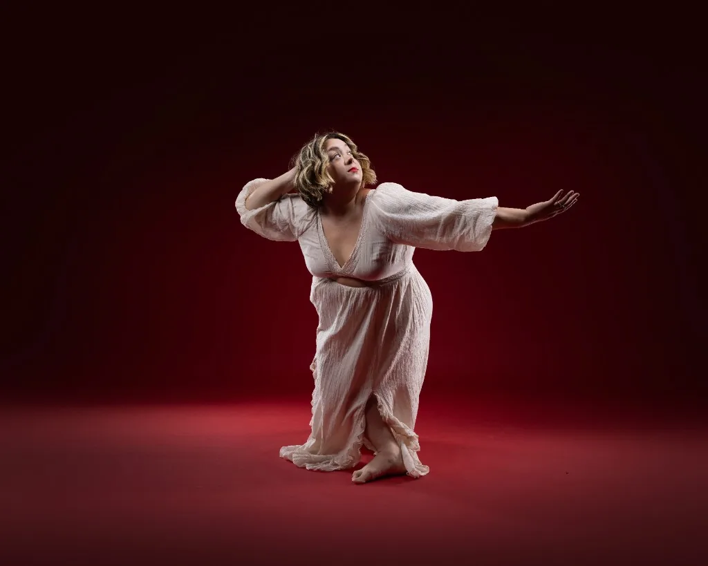 Portrait of Brie Underwood-Duemig in a flowing white dress against a deep red backdrop
